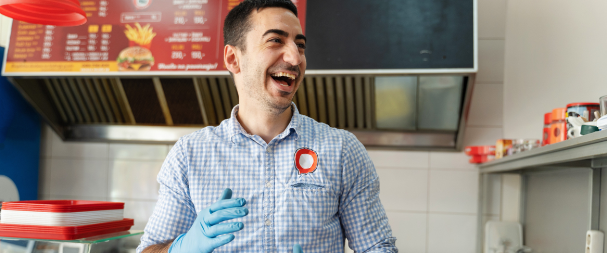 Ein Mitarbeiter eines Fast Food Restaurants steht hinter der Theke und hat sichtlich Freude an seiner Arbeit