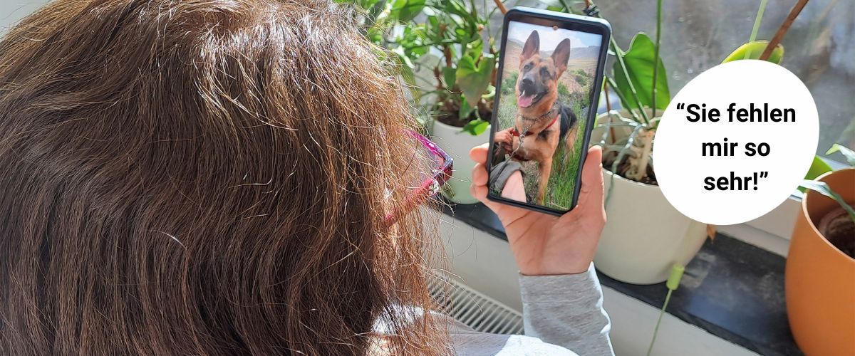 Frau ist von hinten zu sehen und schaut auf ein handy mit dem Foto ihres Hundes