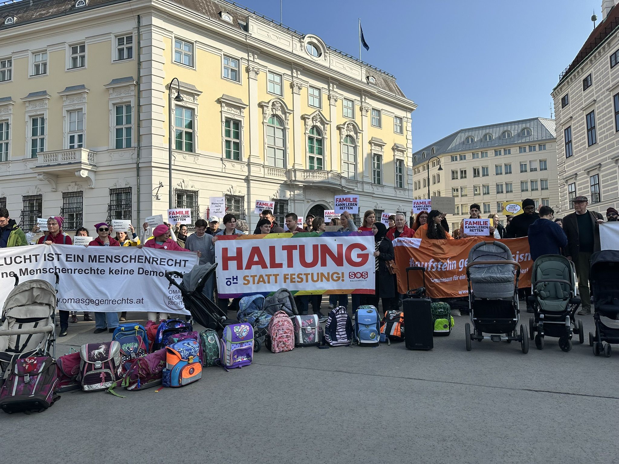 Foto von der Protestaktion vor dem bundeskanzleramt. Menschen mit Bannern, davor Schultaschen und Kinderwägen