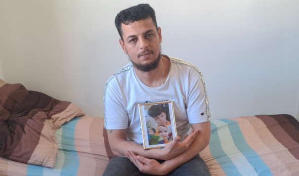 Bewohner im Ute Bock Haus Aadil sitzt mit einem Foto seiner drei Kinder auf dem Bett.