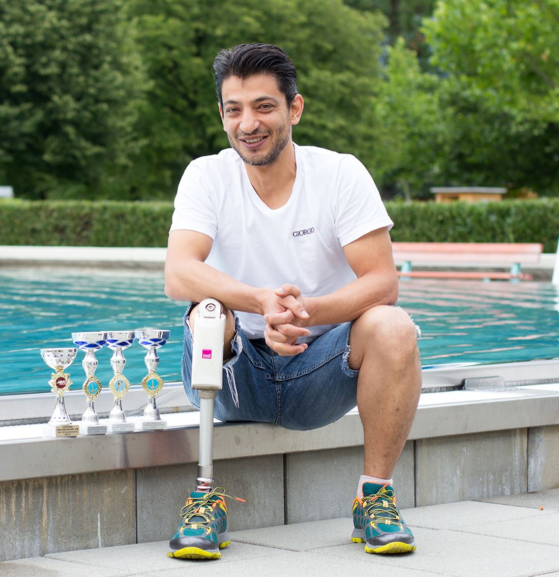 Kami Shahi sitzt an einem Schwimmbecken mit seinen Trophäen