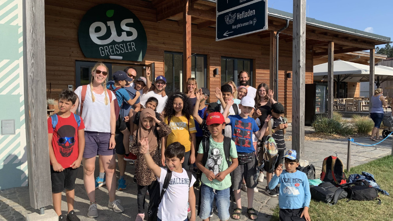 Mitarbeiter*innen von credi2 gemeinsam mit den Kindern aus der Lernbetreuung vom Ute Bock Bildungszentrum steht vor einem Eis-Greissler Schild