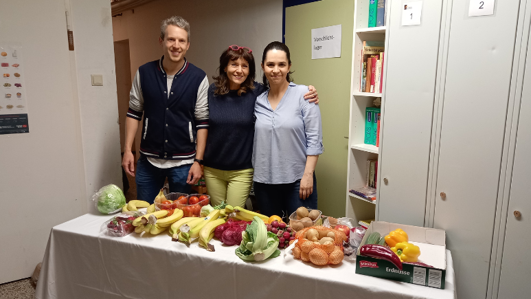 Zwei Mitarbeiterinnen und 1 Mitarbeiter von MSD stehen hinter einem Tisch voll mit Obst udn Gemüse
