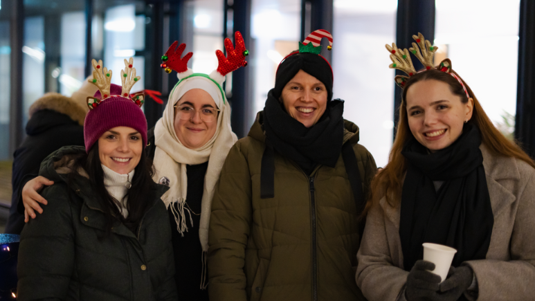 Vier Mitarbeiterinnen von BDO stehen mit dicken Winterjacken und weihnachtlichen Haarreifen draußen, eine hält einen Punsch-Becher