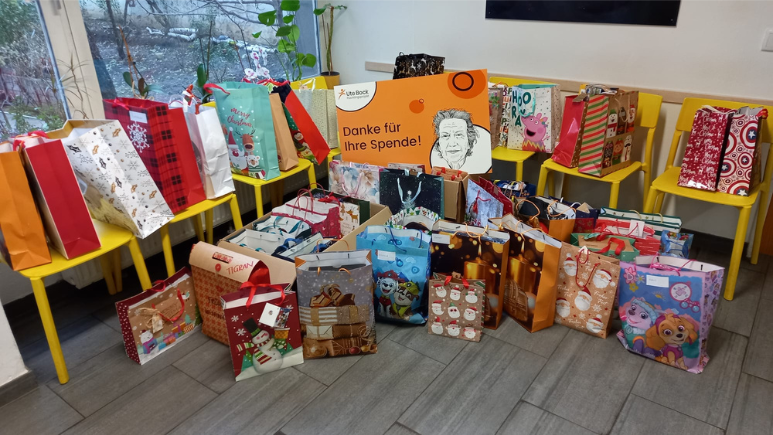 Viele weihnachtsliche Geschenksackerl stehen auf Stühlen und am Boden