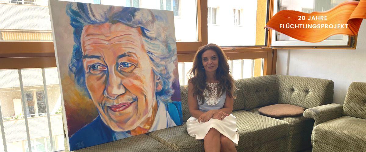 Shirin sitzt neben dem Bild von Frau Bock auf einem Sofa im Ute Bock Haus