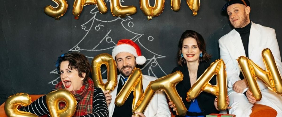 Zwei Frauen und zwei Männer von Salon Spontan stehen vor einer schwarzen weihnachtlichen Wand. In Luftballons ist zu lesen "Salon Spontan""