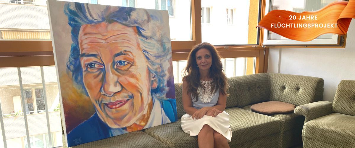 Shirin sitzt neben dem Bild von Frau Bock auf einem Sofa im Ute Bock Haus
