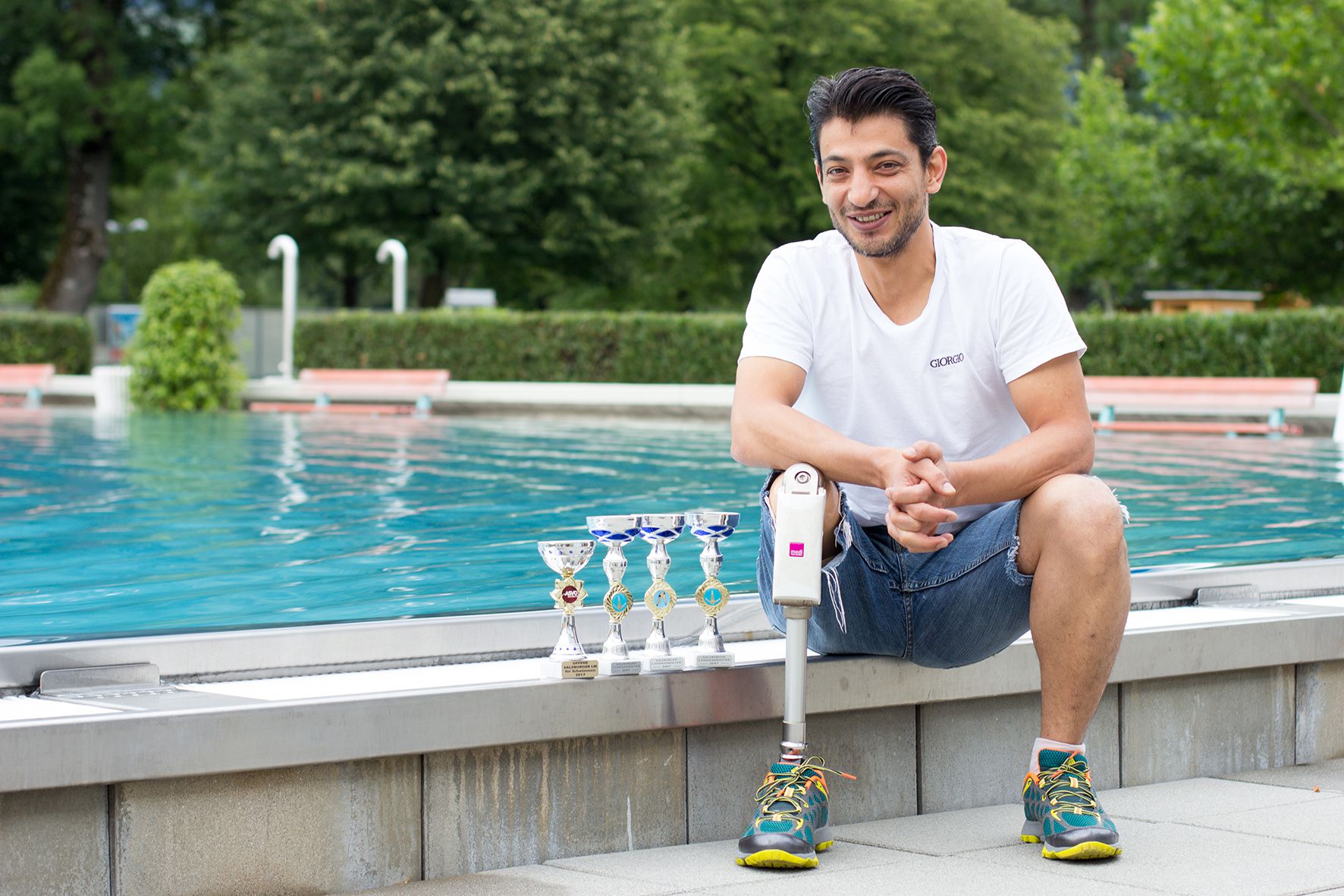 Mann sitzt am Swimming-Pool, neben ihm Trophäen