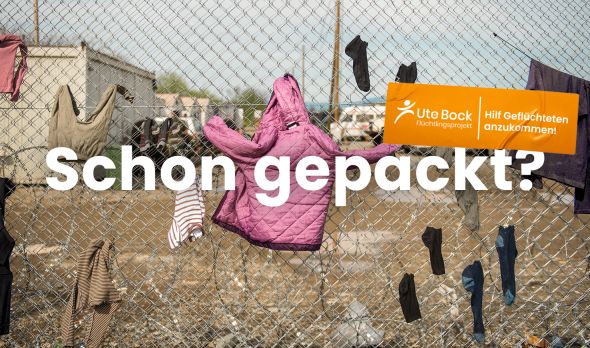 Schriftzug "Schon gepackt?" über Kleidung an Zaun in Flüchtlingsheim