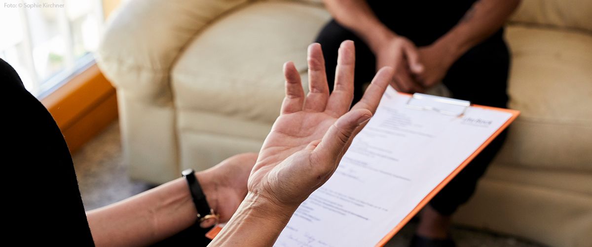 Nahaufnahme Hand und Clipboard in Erklärsituation mit Klient im Hintergrund