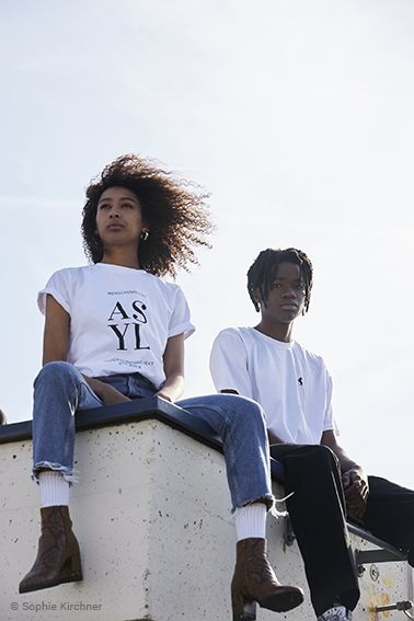 Junge Frau und junger Mann sitzen in Bock Shirts auf einem Dach
