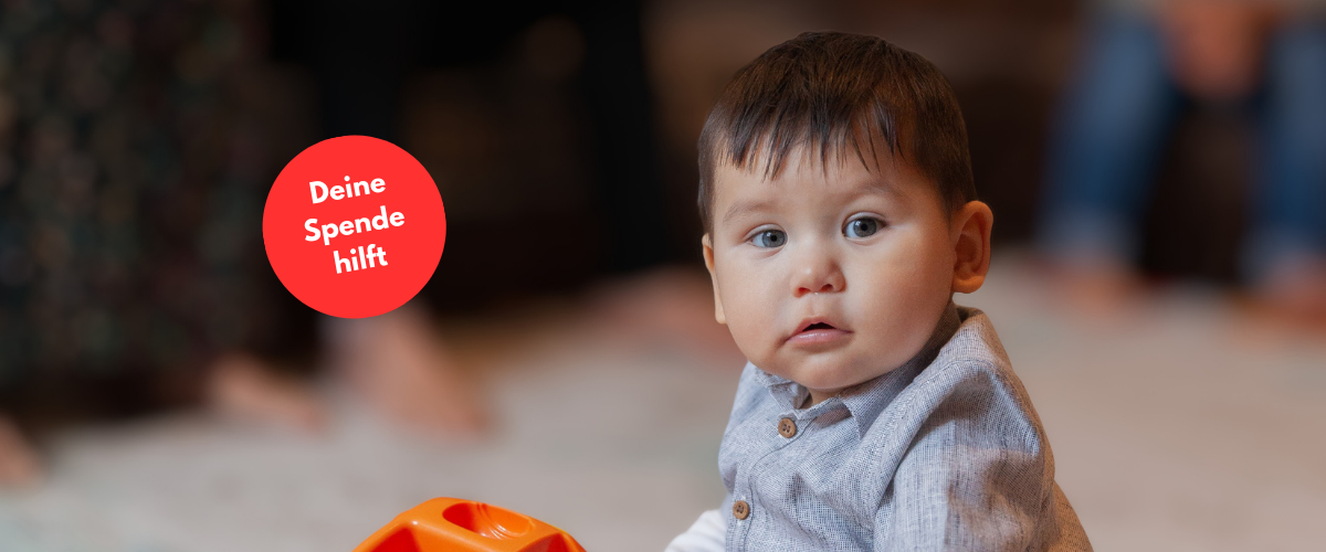 Kleinkind sitzt am Boden und spielt mit einem Plastikspielzeug. Es schaut direkt in die Kamera. Daneben eine rote Bubble "Deine Spende hilft"
